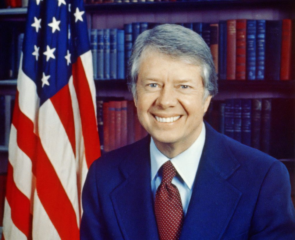 Jimmy Carter, head-and-shoulders portrait, facing front, next to an American flag